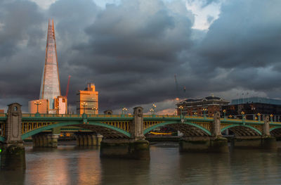 Bridge over river in city against cloudy sky