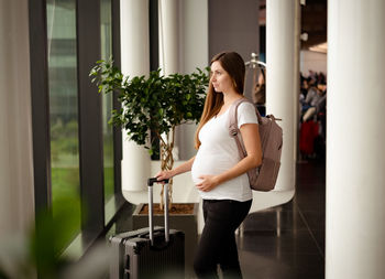 Caucasian brunette young pregnant woman,tourist on holiday with suitcase in airport 