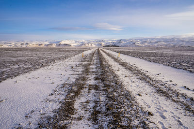 Road amidst snowcapped landscape against sky during winter