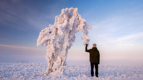 Rear view of man holding frozen tree and snow on field during sunset