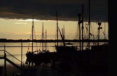 Boats moored in harbor at sunset