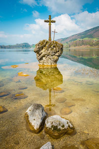 Cross on rock by lake against sky