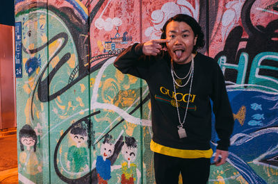 Full length of young man standing against graffiti wall