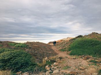 Distant view of couple walking on field against cloudy sky