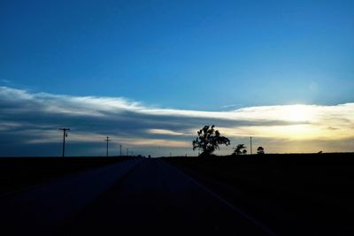 Road amidst silhouette landscape against blue sky during sunset