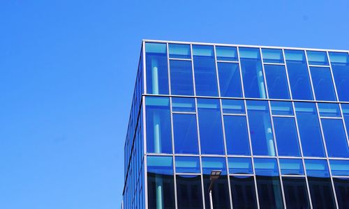 Low angle view of glass building against clear blue sky