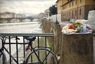 Bicycle on railing by river in city against sky