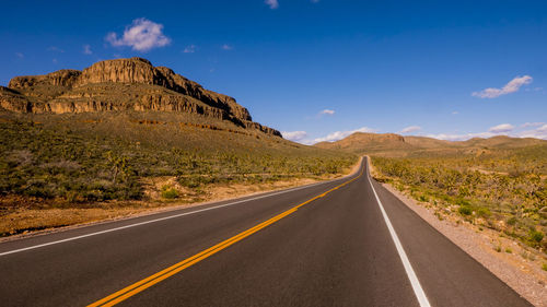 Road leading towards mountains against sky