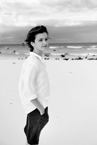 Portrait of teenager standing at beach against sky