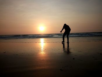 Silhouette man on beach against sky during sunset