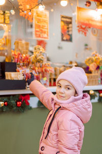 Little happy girl in pink at christmas fair. people buy gifts for holiday at christmas market