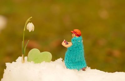 Close-up of figurine by snowdrop flower on snow