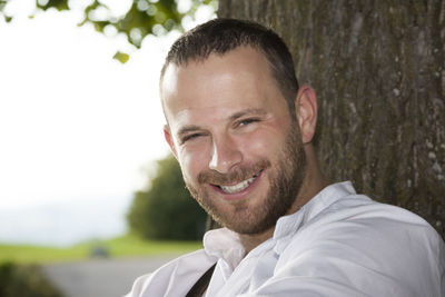 Close-up portrait of smiling man against tree trunk