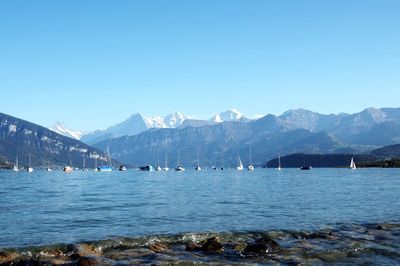 Scenic view of sea by snowcapped mountains against clear blue sky