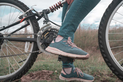 Detail of the feet of a young woman wearing blue pants and sports shoes on the pedals of her bicycle