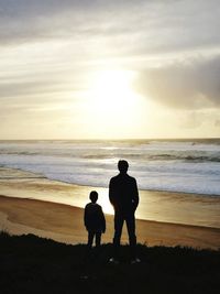 Silhouette children playing on beach against sky during sunset