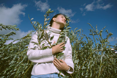 Low angle view of woman holding while standing by plants against sky