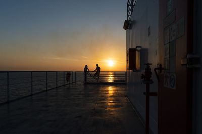 Silhouette people standing by sea against sky during sunset