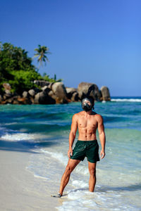 Shirtless man standing on shore at beach