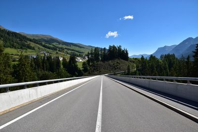 Empty road by trees against sky