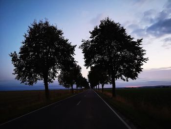 Road amidst trees on field against sky at sunset