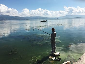 Rear view of man fishing in sea against sky