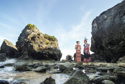 People standing on rock formation against sky