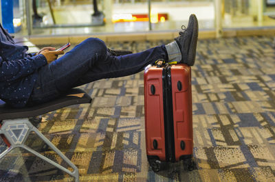 Low section of man using phone sitting with legs on suitcase