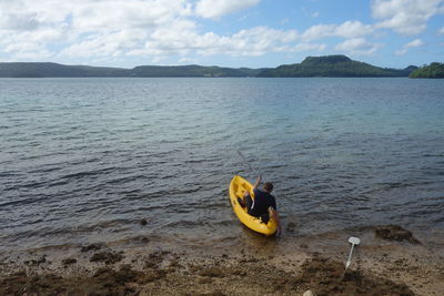 Rear view of man kayaking in sea against sky