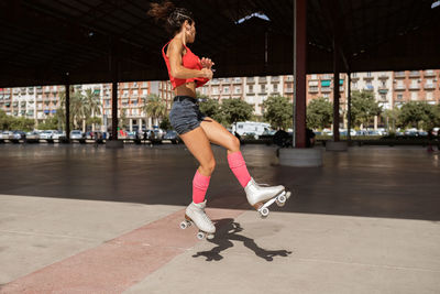 Concentrated female balancing on leg while roller skating on sports ground on sunny day in city