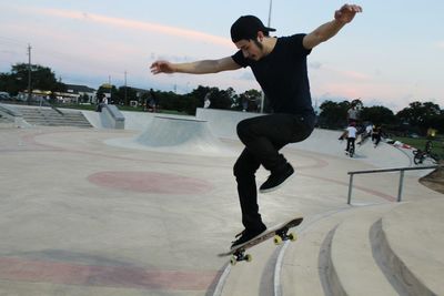 Full length of man with arms outstretched while skateboarding in park