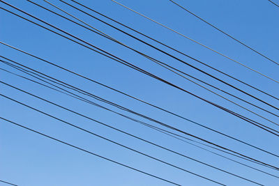 Low angle view of power cables against clear blue sky