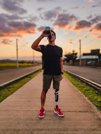 Full length of photographer photographing on railroad tracks against sky during sunset