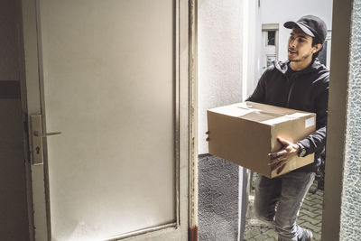 Confident delivery man with package standing at doorstep