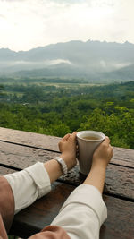Low section of man relaxing on mountain against sky