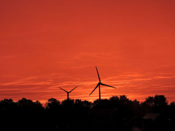 Silhouette of wind turbine against orange sky