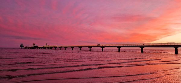 Pier on beach against sky during sunset