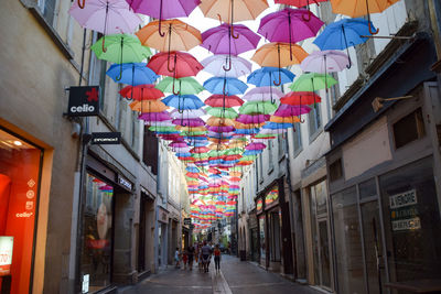 Multi colored umbrellas hanging on street amidst buildings in city