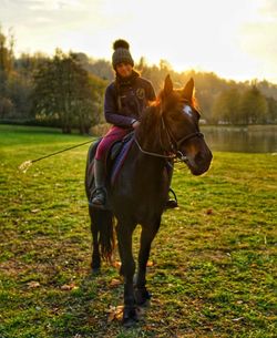 Woman riding horse on field against sky