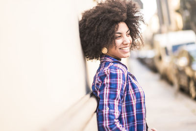 Side view of smiling young woman standing by wall