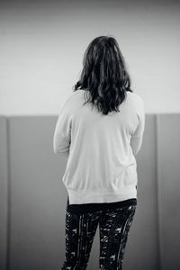 Rear view of woman standing against wall at home