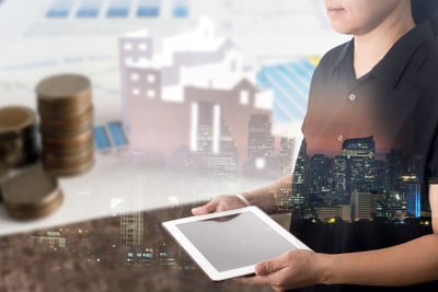 Digital composite image of stacked coins and cityscape with businesswoman holding digital tablet