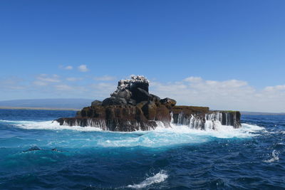 Sea waves splashing on rocks against sky