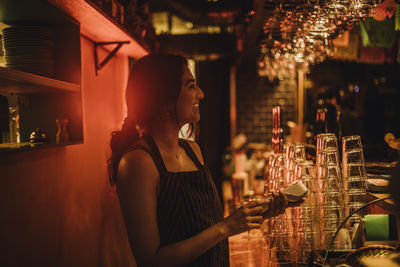 Smiling female bartender holding credit card machine while working at bar