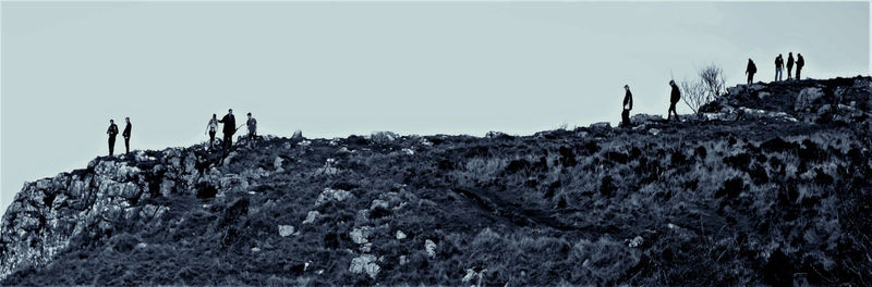 Silhouette people standing on rock by sea against sky