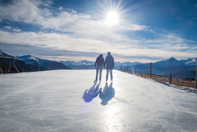 Rear view of man and woman ice skating against sky on sunny day