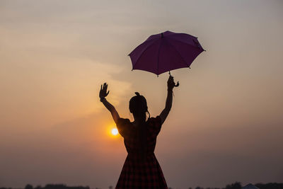 Silhouette woman holding umbrella against sky during sunset