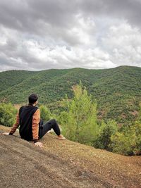 Rear view of man sitting on mountain against sky