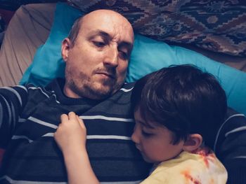 High angle view of father looking at son while lying on bed
