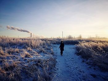 Rear view of woman walking on snow covered field against sky